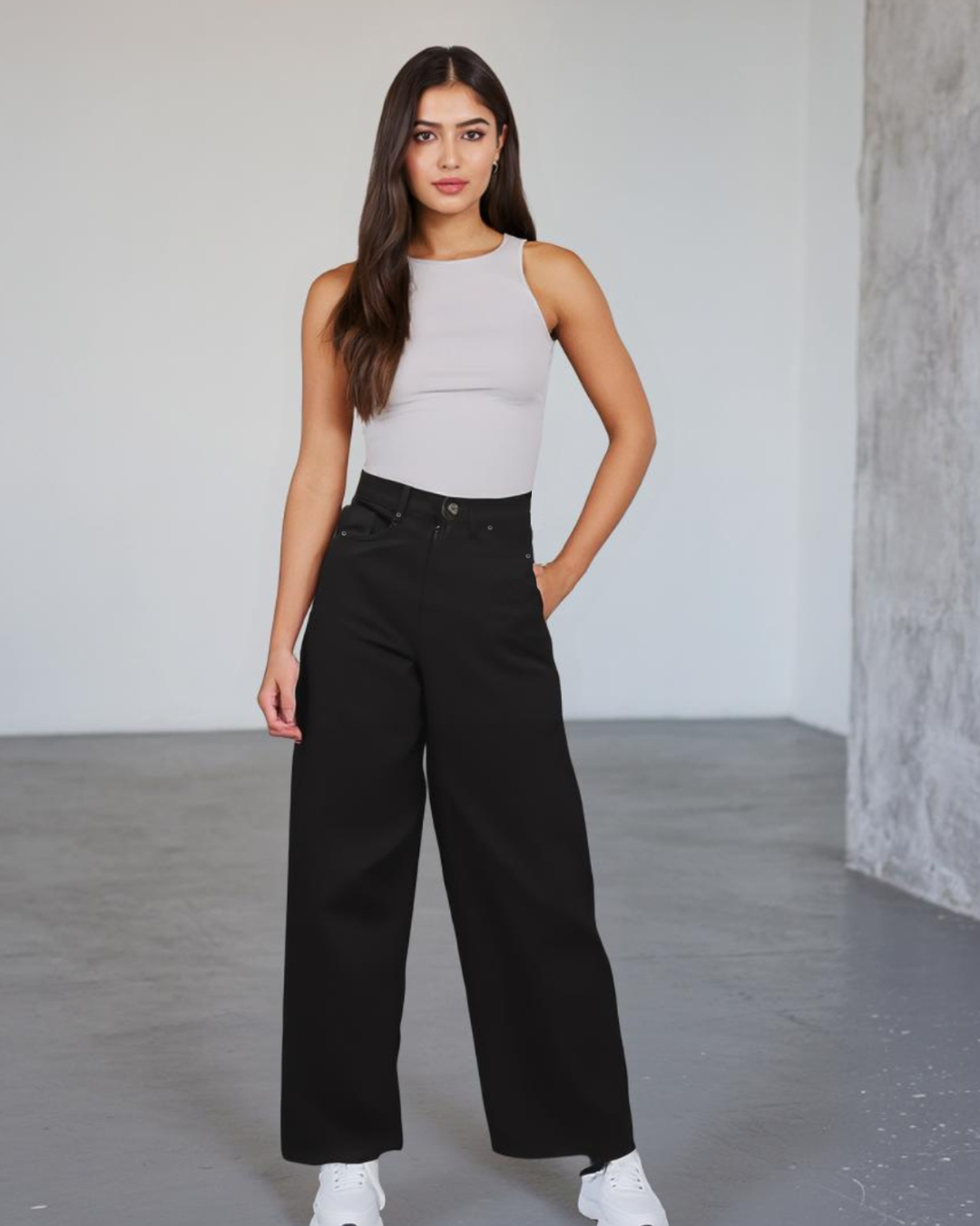 Woman wearing a light gray sleeveless top and black high-waisted pants in a minimalistic setting.