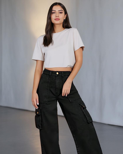Woman wearing a white crop top and black cargo pants against a plain background